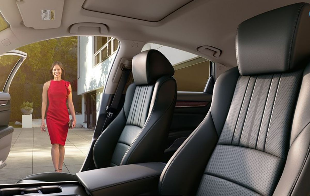 Black interior of a Honda Accord Touring with black leather seats that are heated and ventilated. The passenger-side door is open and you can see a white woman in a red dress walking toward the car