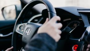 Close up of hands on a Honda steering wheel. The new HondaTrue Used certified pre-owned program can help more drivers get into older model year Honda cars