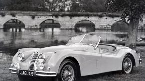 A white 1954 Jaguar XK140 Roadster parked next to a river bridge