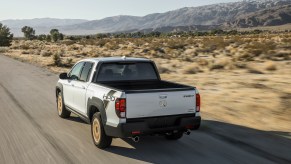 White Honda Ridgeline driving down a road in the desert.