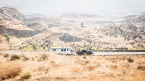 A pickup truck in the distance pulls an airstream trailer through the mountains, sandy ridgelines visible behind it.