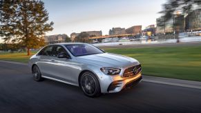 Silver Mercedes-Benz E-Class Sedan driving along a smooth road in a city, alongside a small pond