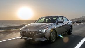 The 2022 Hyundai Elantra Hybrid compact sedan driving down a seaside highway at sunset