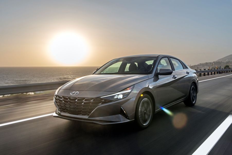 The 2022 Hyundai Elantra Hybrid compact sedan driving down a seaside highway at sunset