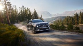 The front 3/4 view of a brown 2022 Hyundai Santa Fe Hybrid driving down a mountain forest dirt road