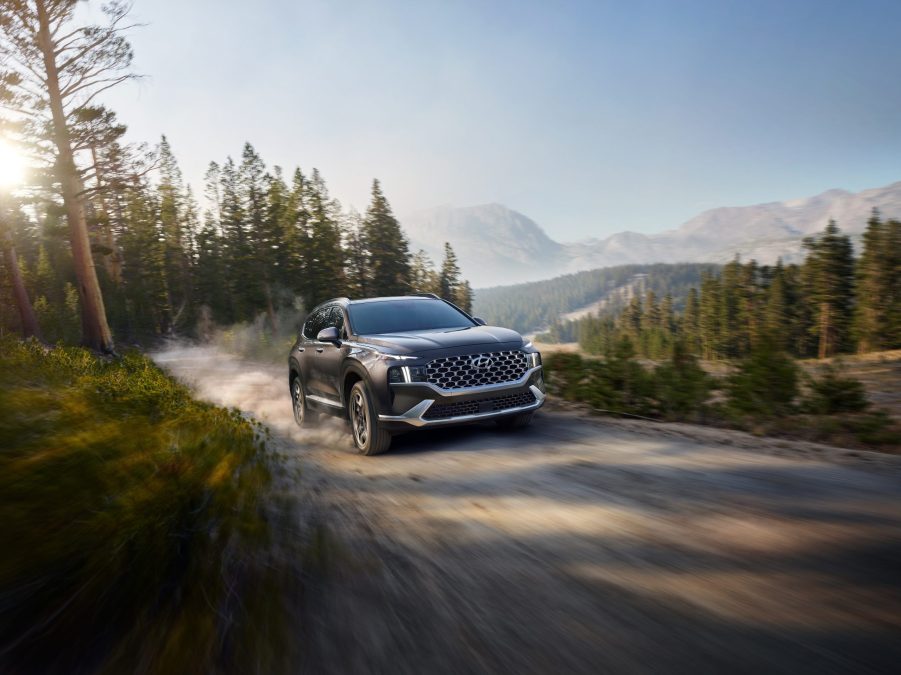 The front 3/4 view of a brown 2022 Hyundai Santa Fe Hybrid driving down a mountain forest dirt road