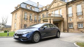 A blue 2022 Mercedes-Benz EQS in front of a large brown brick house.