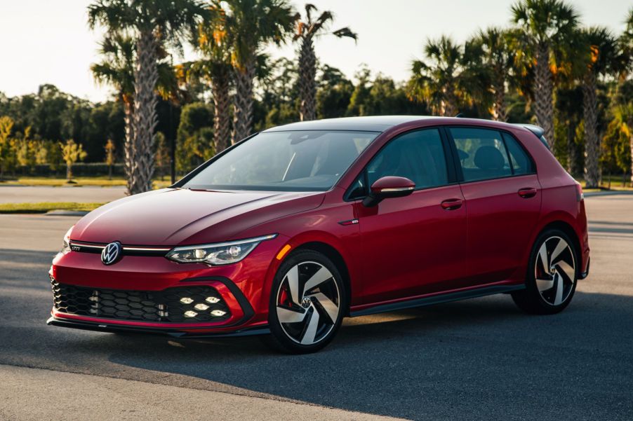 The 2022 Volkswagen Golf GTI sporty hot hatch hatchback in red parked on an asphalt lot surrounded by tropical trees