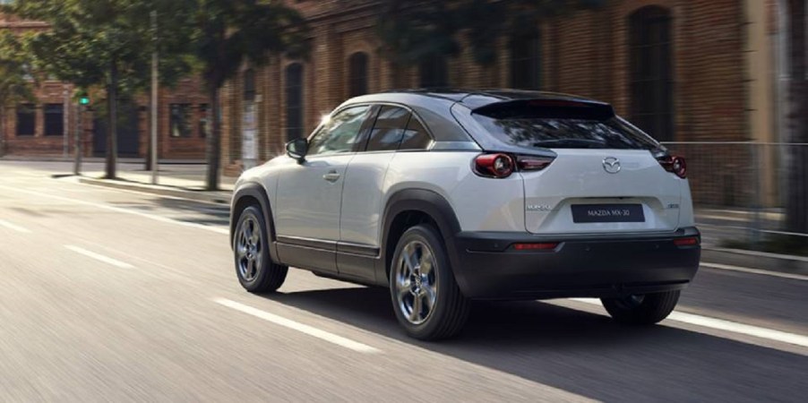 A white 2022 Mazda MX-30 driving down a city road.