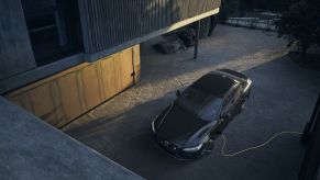 A black Volvo S60 Recharge Plug-In Hybrid sedan parked in a driveway and attached to a charging plug