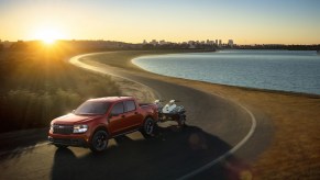 A red 2022 Ford Maverick tows a small boat on a waterfront road.