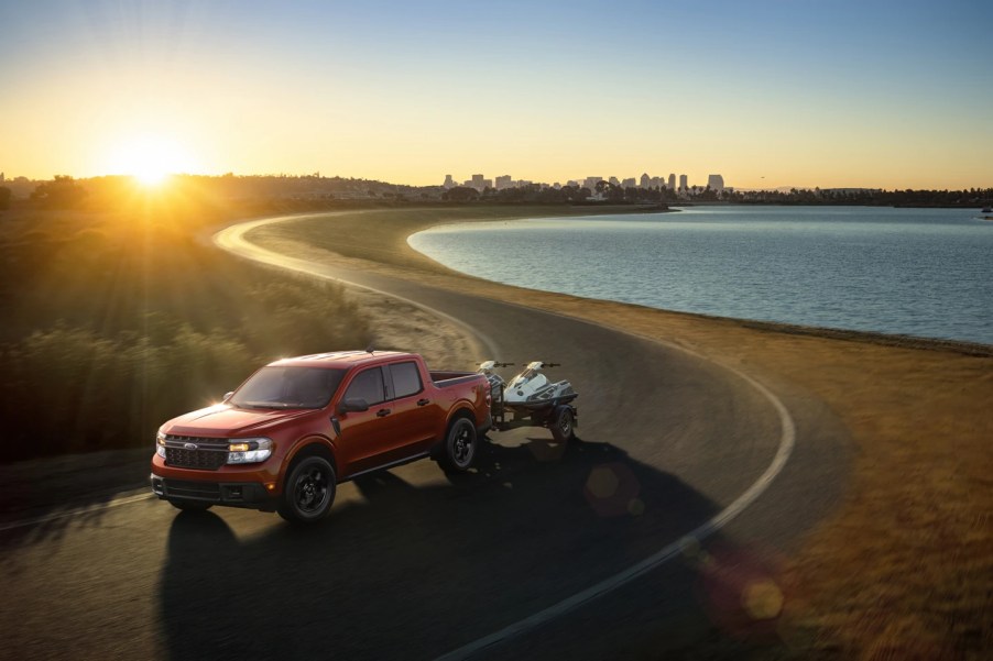 A red 2022 Ford Maverick tows a small boat on a waterfront road.