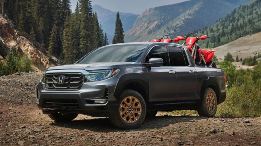 A 2022 Honda Ridgeline traversing a dirt road hauling two dirt bikes demonstrating its midsize pickup truck capabilities.