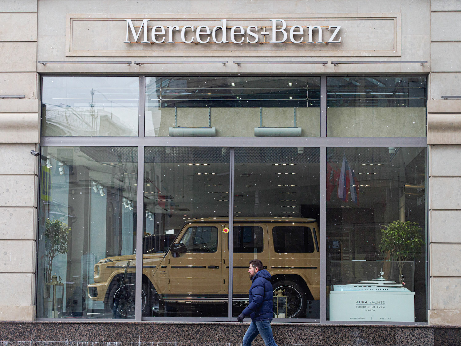 Tan Mercedes G Wagon SUV in a dealership window on a city street.