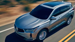 A silver 2022 Acura RDX small SUV is driving on the road.