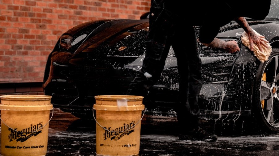 A man washing a black car using two bucks and a soft wash mitt to avoid unecessary damage