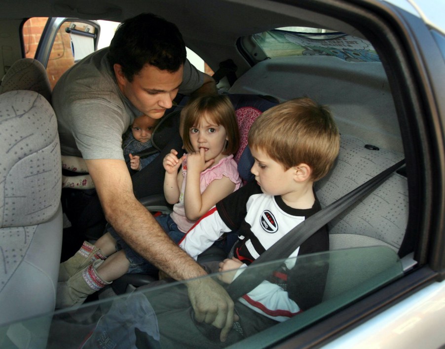 A dad buckles his kids into the back seat of a car.