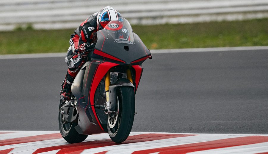 A black-clad rider taking the red-and-black Ducati V21L MotoE electric motorcycle prototype around a track