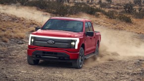 A red 2022 Ford F-150 Lightning electric pickup truck is driving off-road.