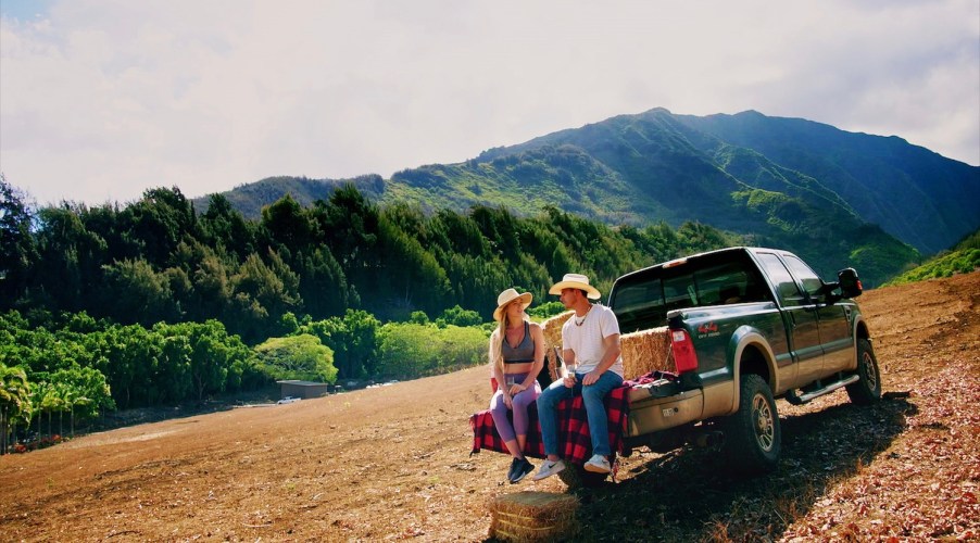 Couple sitting on the tailgate of a Ford F-150 pickup truck, a range of mountains in the background.