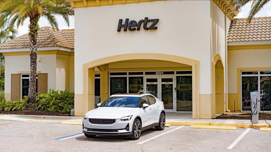 White Polestar 2 electric vehicle parked in front of a tan Hertz building.