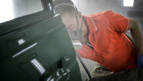 Technician spraying primer and green paint onto a car door.