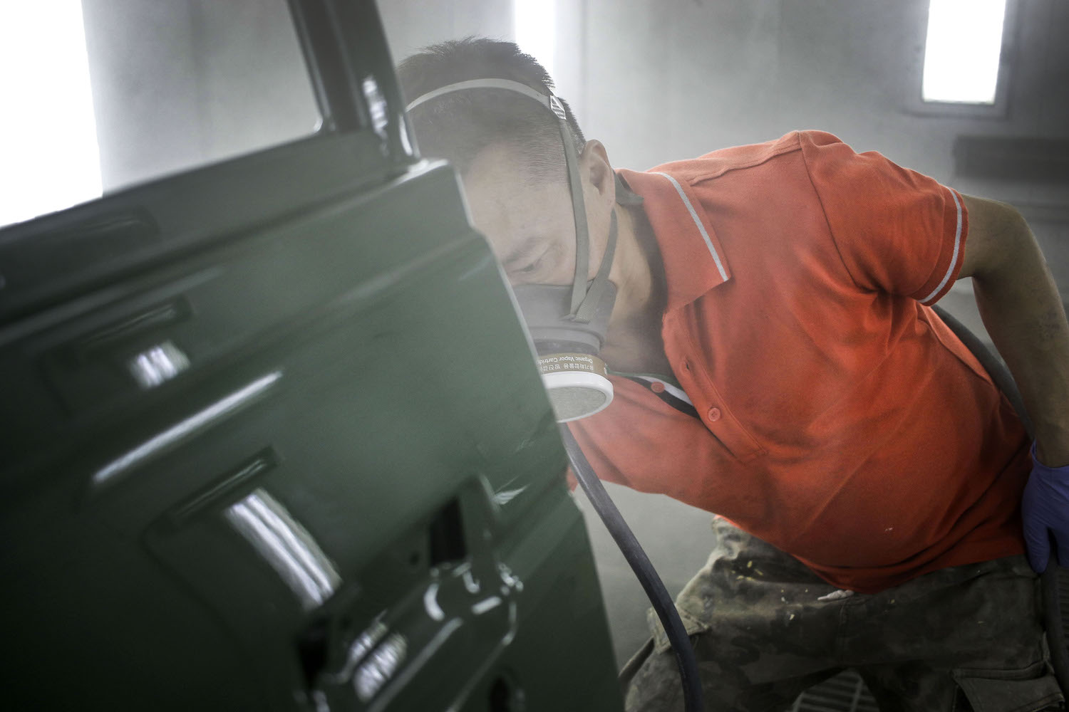 Technician spraying primer and green paint onto a car door.