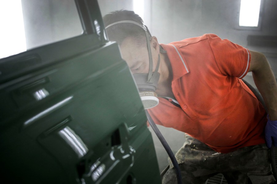 Technician spraying primer and green paint onto a car door.