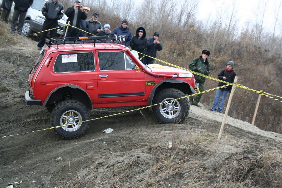 A red Lada Niva shows off its off-road capability as a 4x4 SUV on a dirt road.