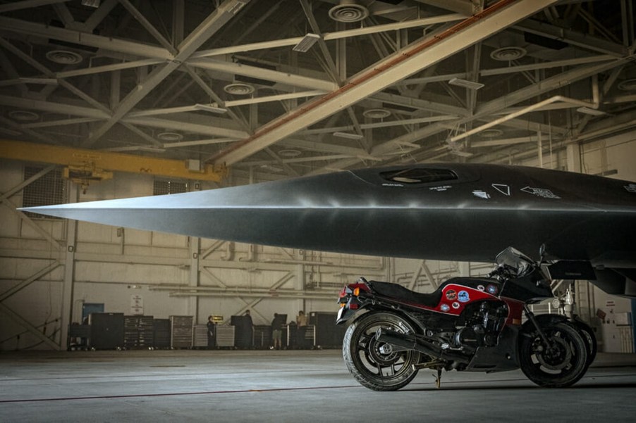 Maverick's red-and-black 1986 Kawasaki Ninja 900 by a gray fighter jet on the Top Gun: Maverick set