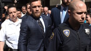 Connor McGregor wearing a suit being escorted by police to court date