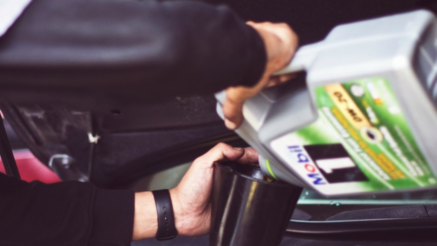 A man refills the engine's oil with a funnel and the proper oil