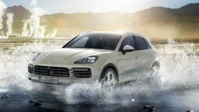 A white 2022 Porsche Cayenne E-Hybrid luxury hybrid SUV is driving through the water.