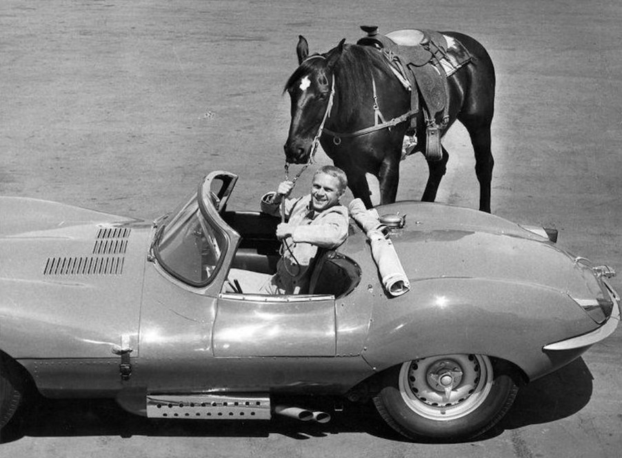 Steve McQueen in a convertible holding the reigns of a horse