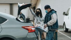 Folks loading a box of groceries into a sedan's open trunk area