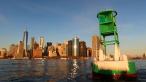 A green buoy covered in ice in the New York Harbor area of lower Manhattan and the One World Trade Center