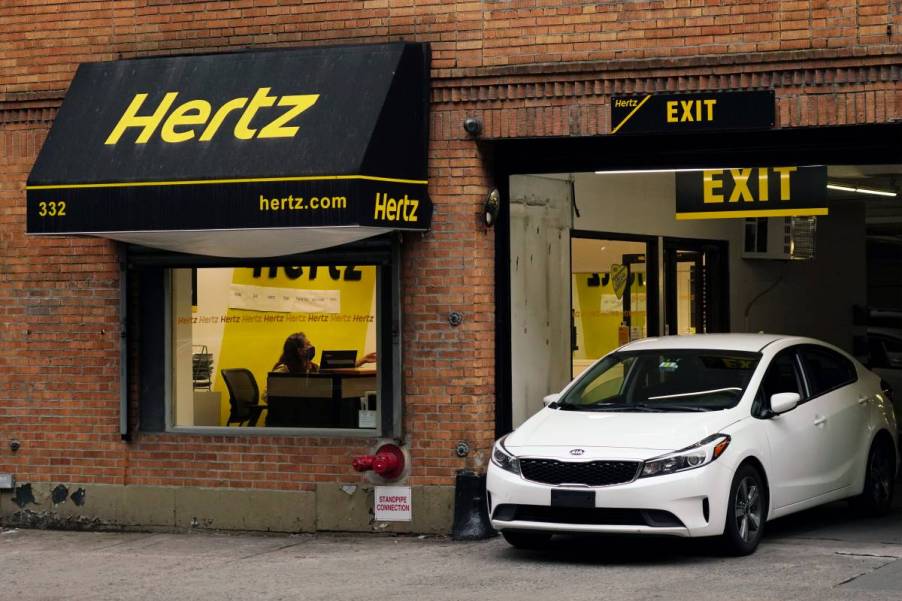 A white rental car drives out of a Hertz rental car company location in New York City