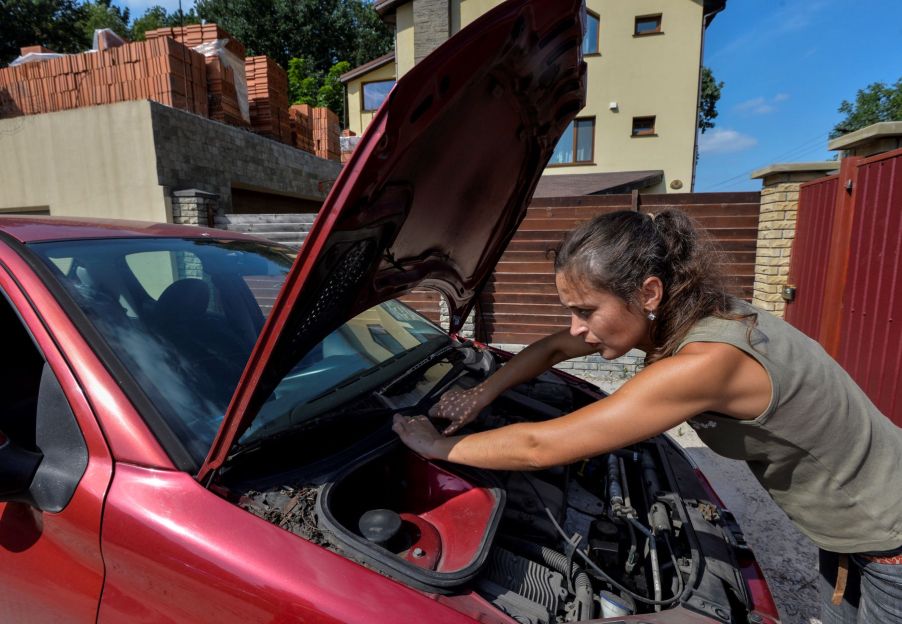 A woman inspecting and performing maintenance on her car engine under the hood of her vehicle in Kiev, Ukraine