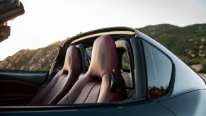 Close-up shot of the driver and passenger seats in a Mazda Miata with the top down. There's a small panel behind the seats to allow for air flow