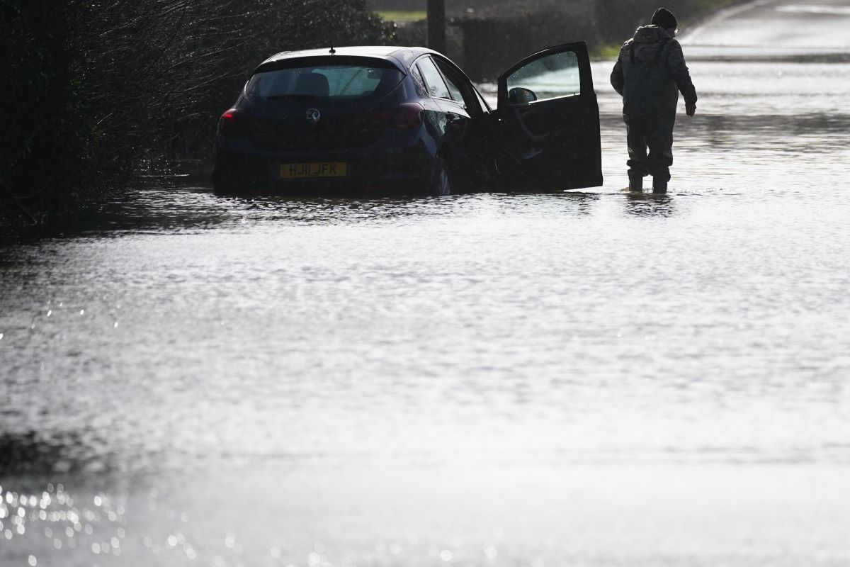 A small blue hatchback stuck in high water, its driver wading away from the vehicle. Flood damage does not make for a reliable used car.