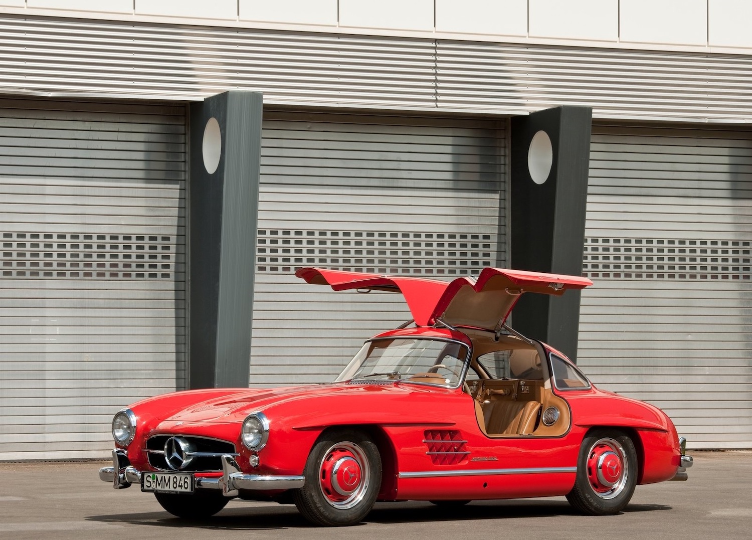 Red 1954 Mercedes-Benz "Gullwing" coupe parked in front of an old Art Deco building with its doors up.