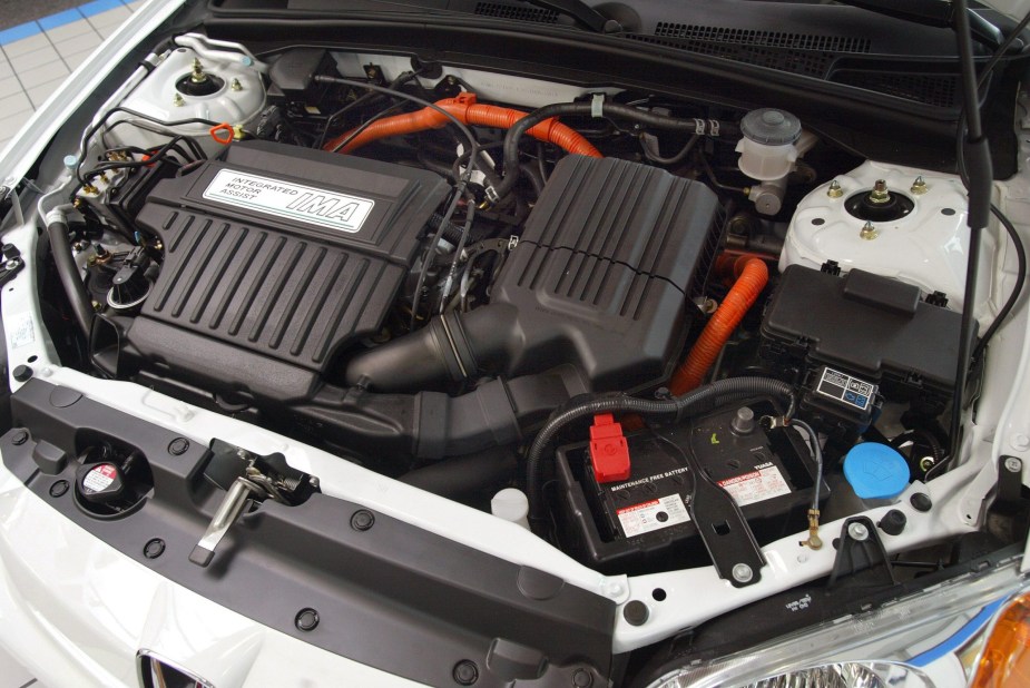 The engine bay of a silver 2003 Honda Civic Hybrid showing its 12-volt lead-acid car battery