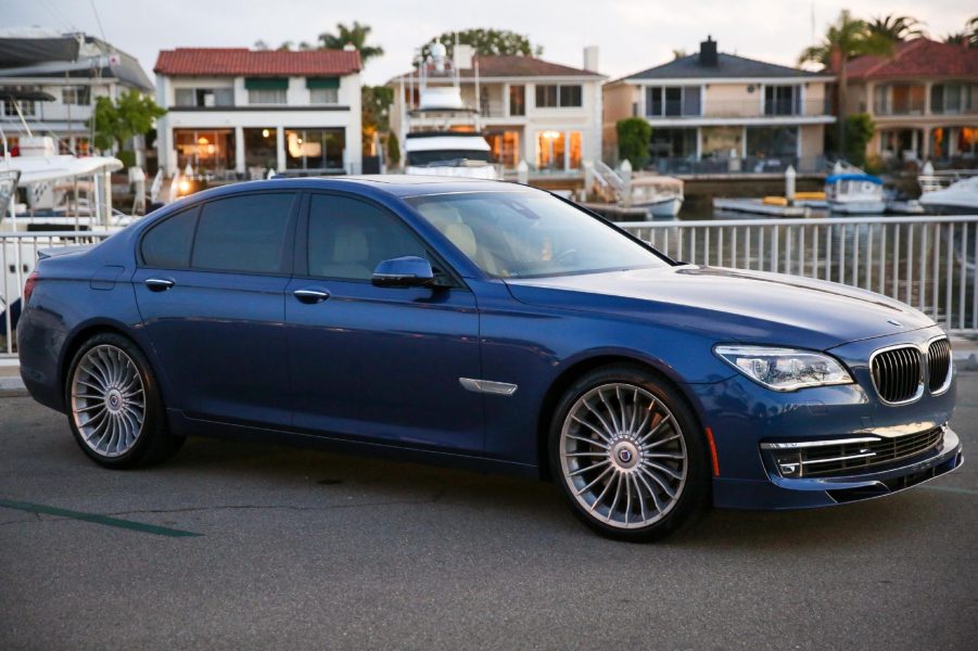 A blue 2014 BMW Alpina B7 with tinted windows by a marina