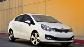 A white 2015 Kia Rio sedan parked next to a yellow wall