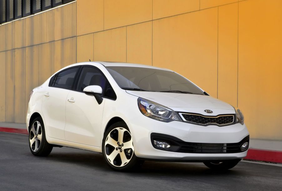 A white 2015 Kia Rio sedan parked next to a yellow wall