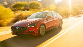 a red 2020 hyundai sonata drives along a road basked in a sunset