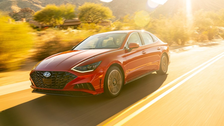 a red 2020 hyundai sonata drives along a road basked in a sunset