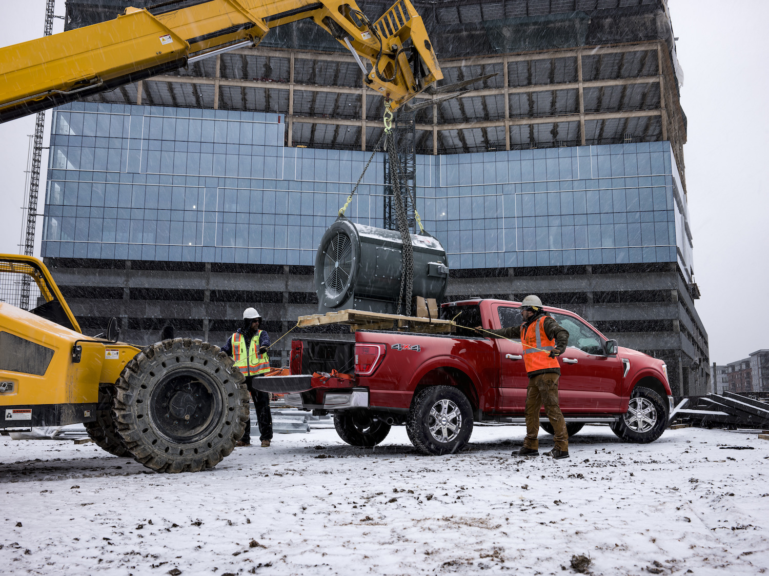 Construction workers setting a heavy piece of equipment in the bed of a half-ton Ford pickup truck.