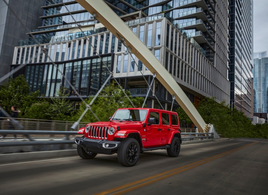 A red Jeep Wrangler 4xe plug-in hybrid driving through a city.