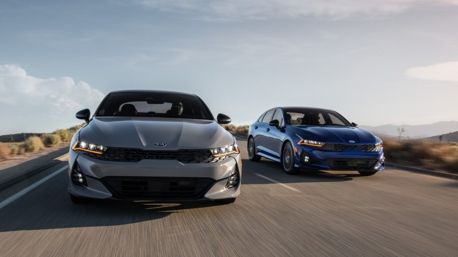 a grey kia k5 gt line and kia k5 gt drive along a road showing off the sleek and modern styling